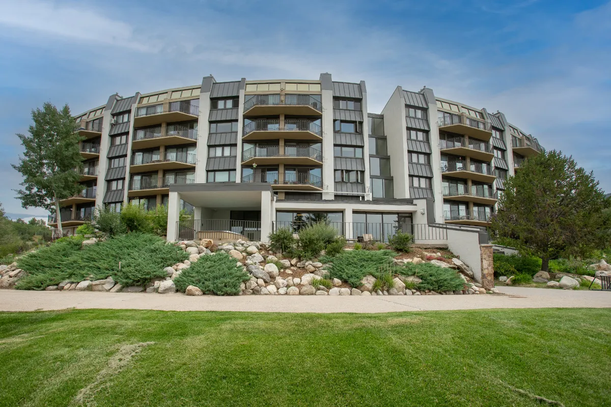 A contemporary exterior view of the condo building with modern architecture, landscaped gardens, and balconies. The garden area is lush and inviting, and the balconies offer scenic views, suggesting a relaxing space for guests year-round.