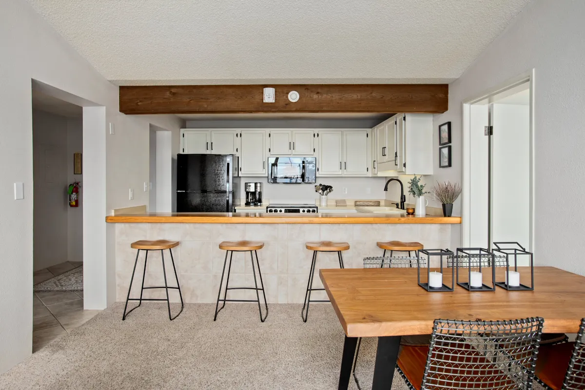 This photo features a well-lit kitchen with a spacious island, bar stools, and a cozy dining table set nearby. The open arrangement allows for seamless transitions between cooking and dining, with space for everyone to join in.