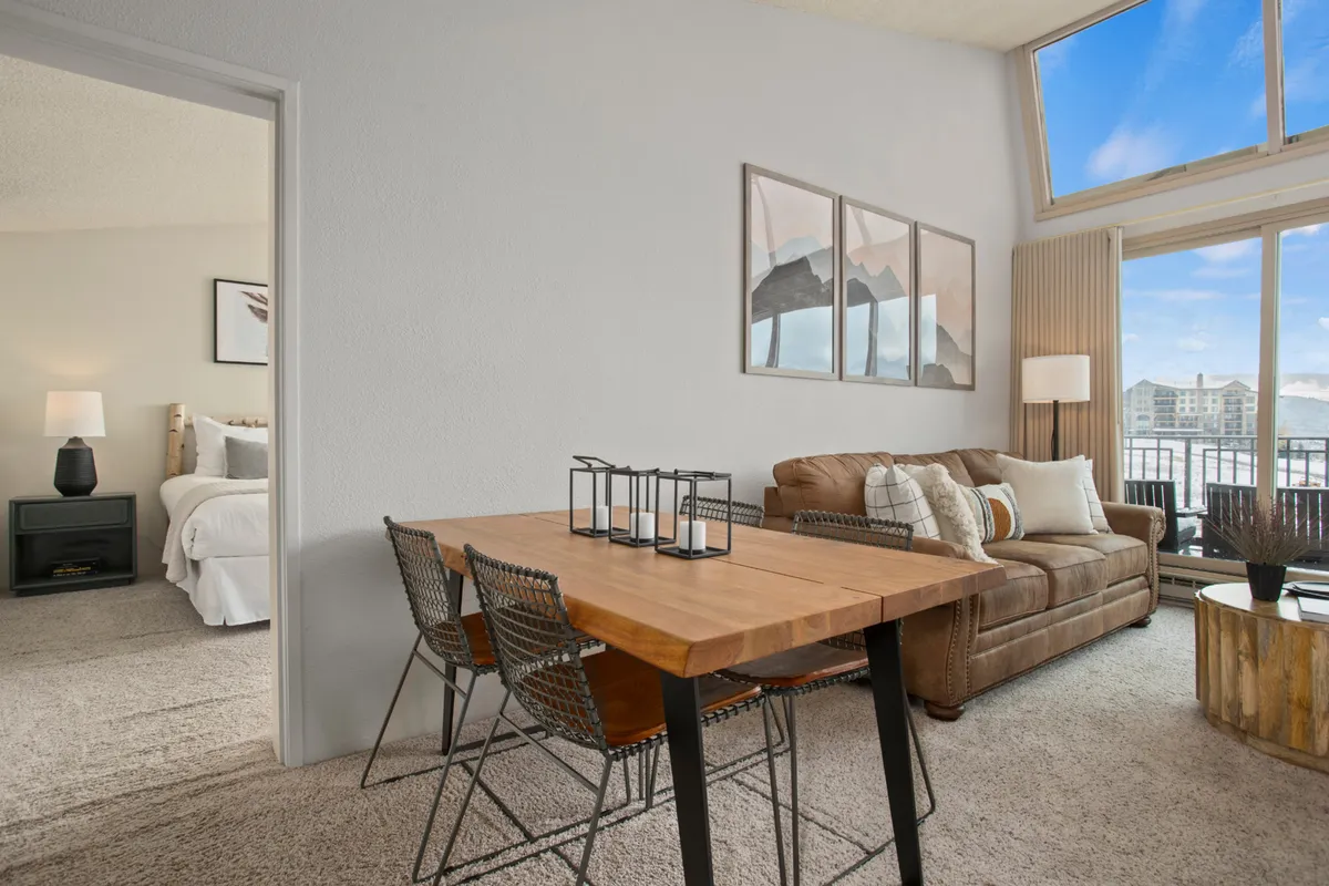An inviting open-concept living and dining area with a stylish sofa and a modern dining table situated next to expansive windows. The layout encourages both relaxation and social interaction, and the view outside frames the snowy mountain landscape.