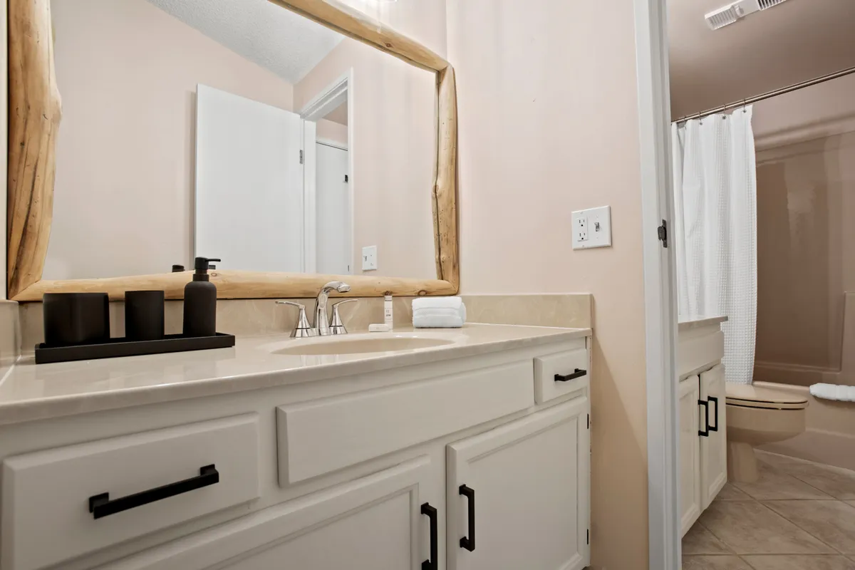 A tastefully designed ensuite bathroom with a natural wood-framed mirror, elegant sink and faucet, and decorative bottles. The serene setting is perfect for morning routines or relaxing after an adventurous day.