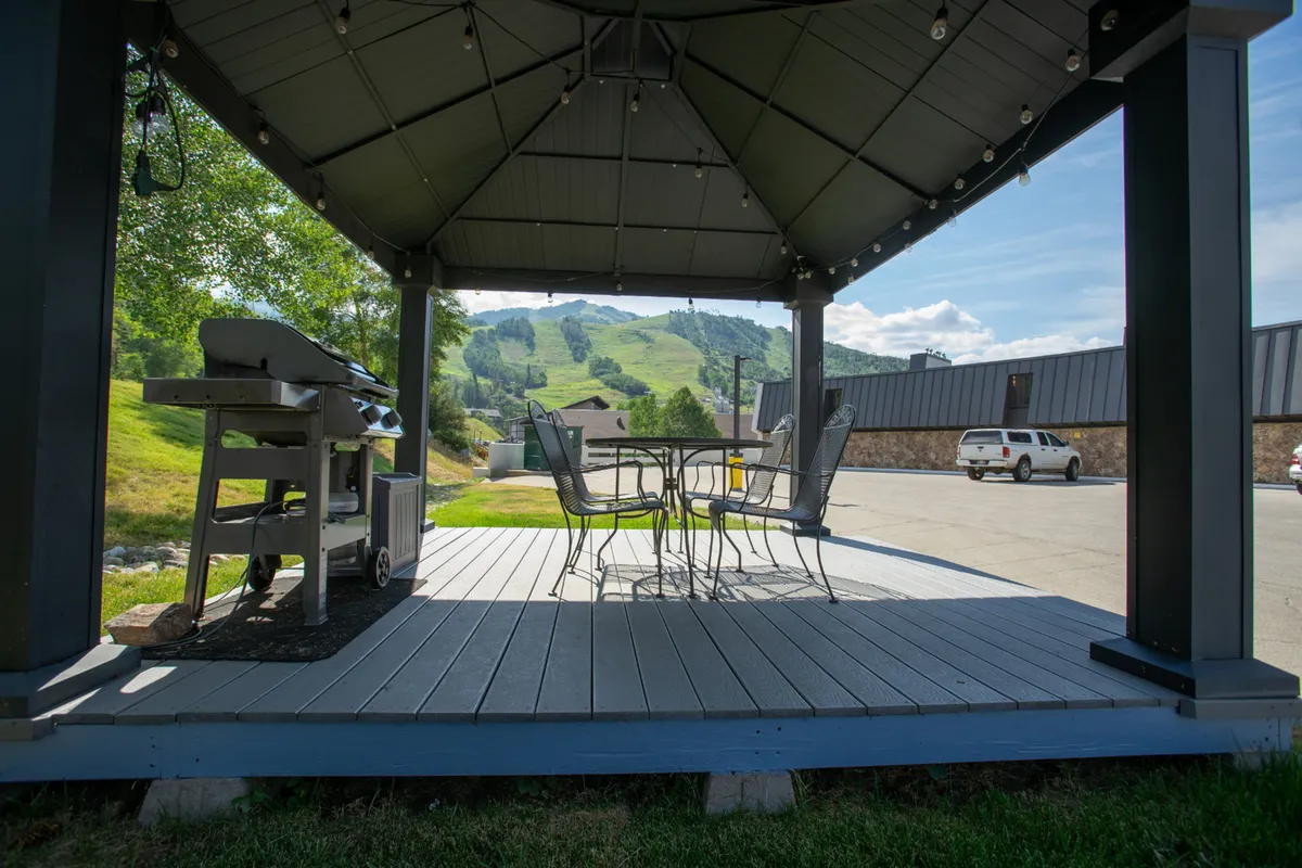 An exterior scene featuring a gazebo with a table and chairs, grill, and expansive mountain views. The area is set up for outdoor dining and casual gatherings, making it a hub for family fun and socializing.