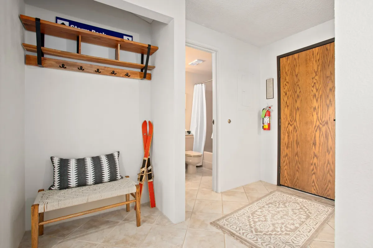 A cozy, functional mudroom or entryway featuring a bench with a decorative pillow, a ski rack with visible skis, and a welcoming door—clearly designed for storing and transitioning winter gear after an active day outside.