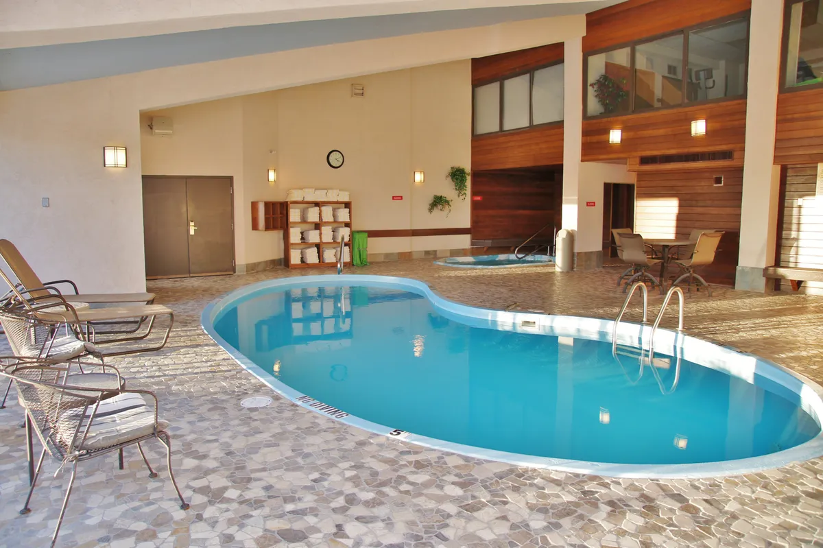 A serene indoor swimming pool area with wooden paneling, neatly arranged lounge chairs, and stacks of towels ready for use. The atmosphere is tranquil and rejuvenating, inviting guests to swim or unwind by the poolside.