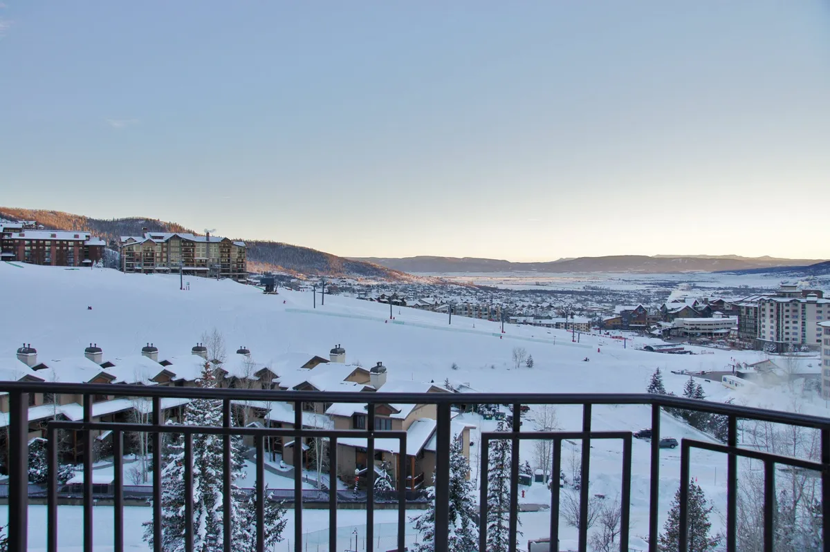 A serene exterior shot at sunset, highlighting snow-covered slopes, majestic mountain ranges, and cozy residential buildings nestled near ski lifts. The tranquil mood is accentuated by soft golden light, hinting at the peaceful side of mountain life after a day of adventure.