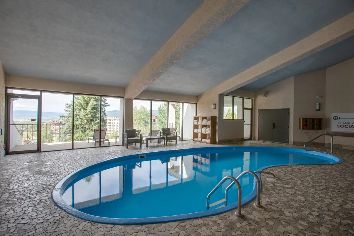 A bright, tranquil indoor swimming pool area with large windows offering sweeping views of the landscape. Comfortable seating is arranged for relaxation, and the pool's clear water beckons for a refreshing swim after a day outdoors.
